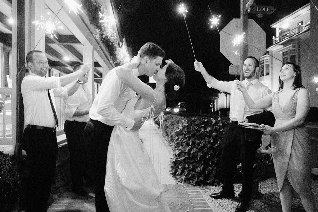 4th of July Wedding: A couple kissing at their wedding reception, and guests holding sparklers next to them.