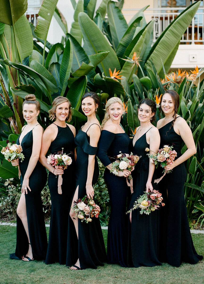 Six bridesmaids in a mix of black dresses pose with their earth tone bouquets and big smiles.