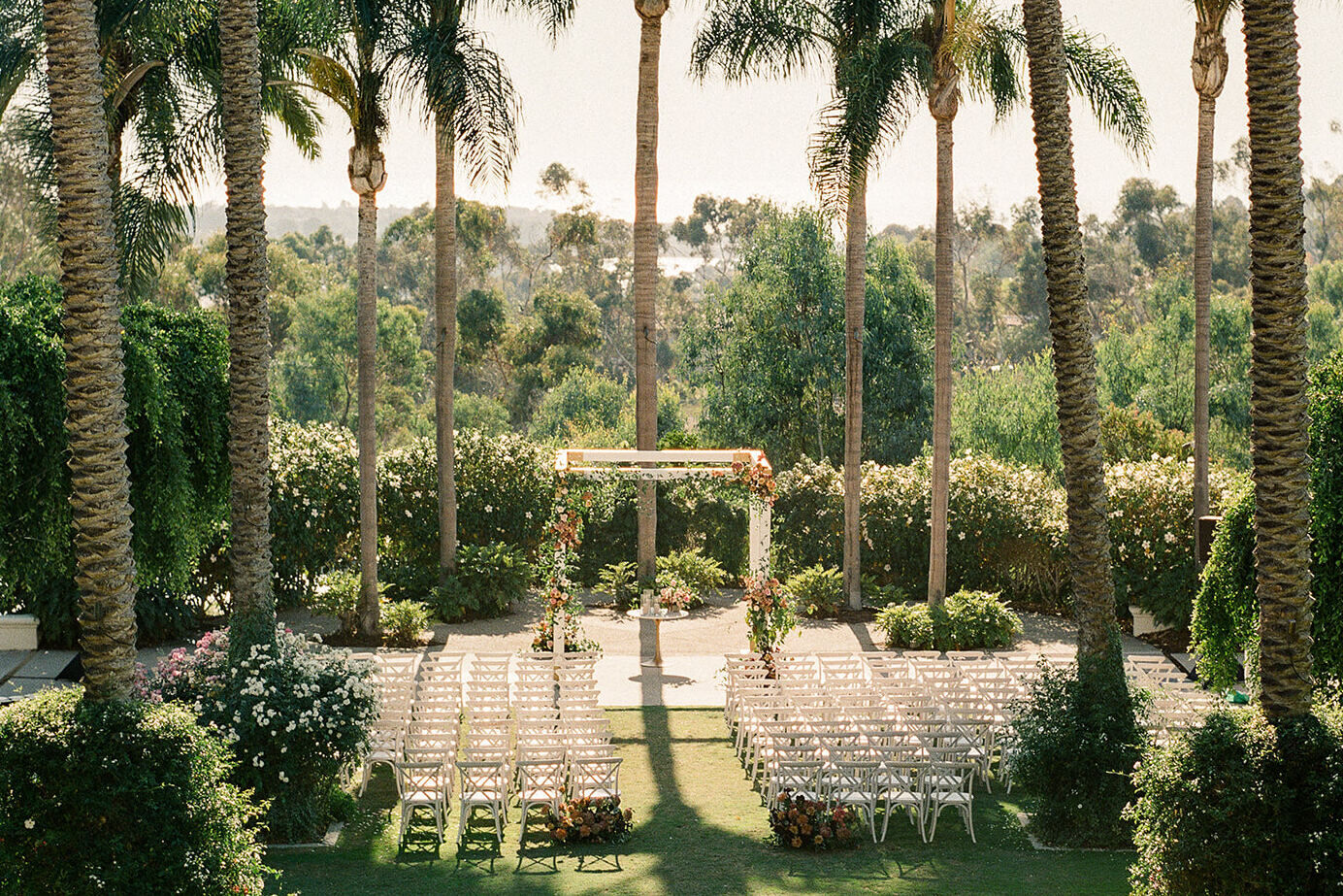 An elevated view of a palm-tree surrounded lawn set up for an outdoor wedding ceremony at the Park Hyatt Aviara Resort in California.