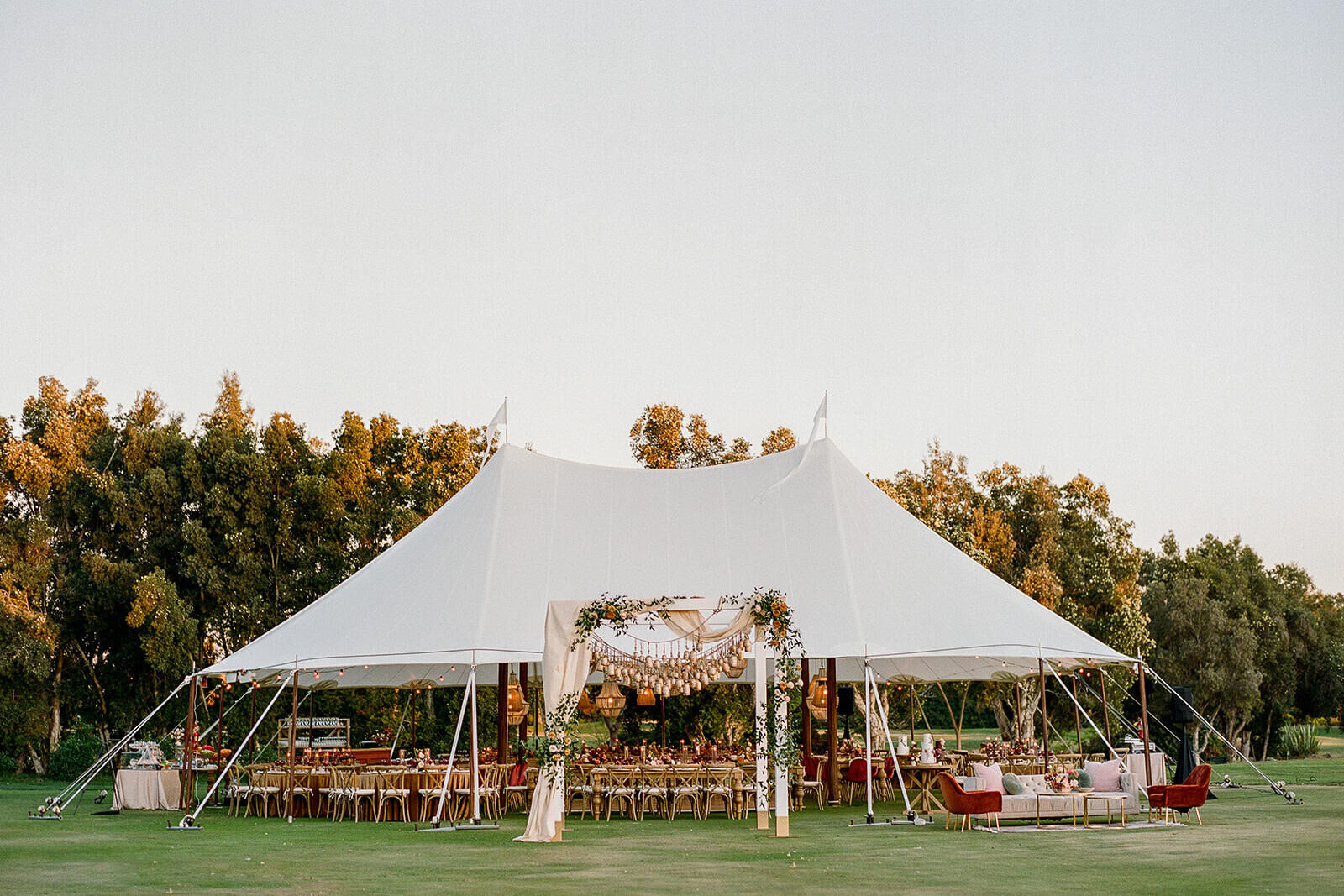 The tented reception at an earth tone wedding, complete with an outdoor seating area and archway holding brass bells that doubled as seating assignments for guests.