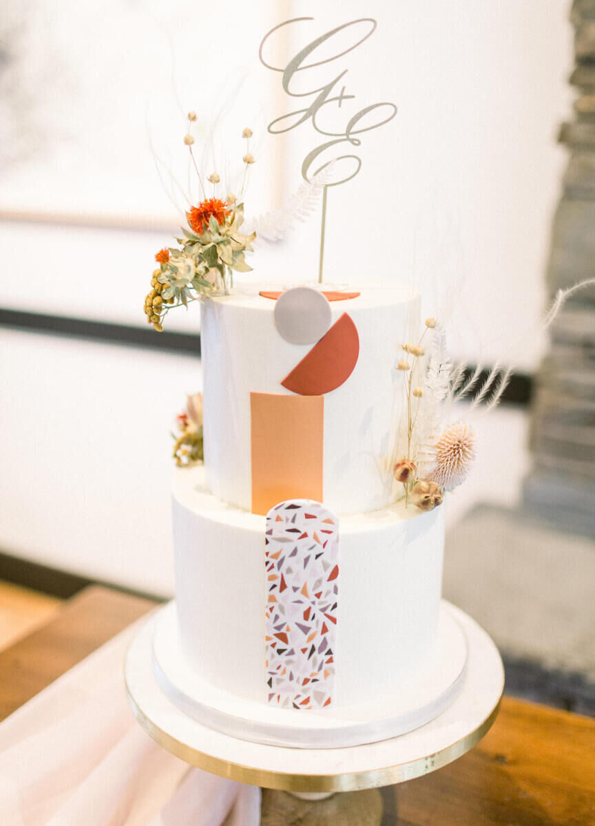 Wedding Traditions: A two-tiered wedding cake with flowers, geometric cut-outs, and the couple's initials.