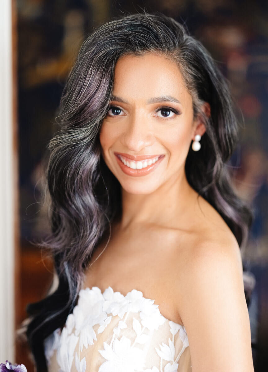A close-up portrait of a bride in a strapless wedding dress with stunning soft waves and a natural makeup application, smiling during her art museum wedding day.