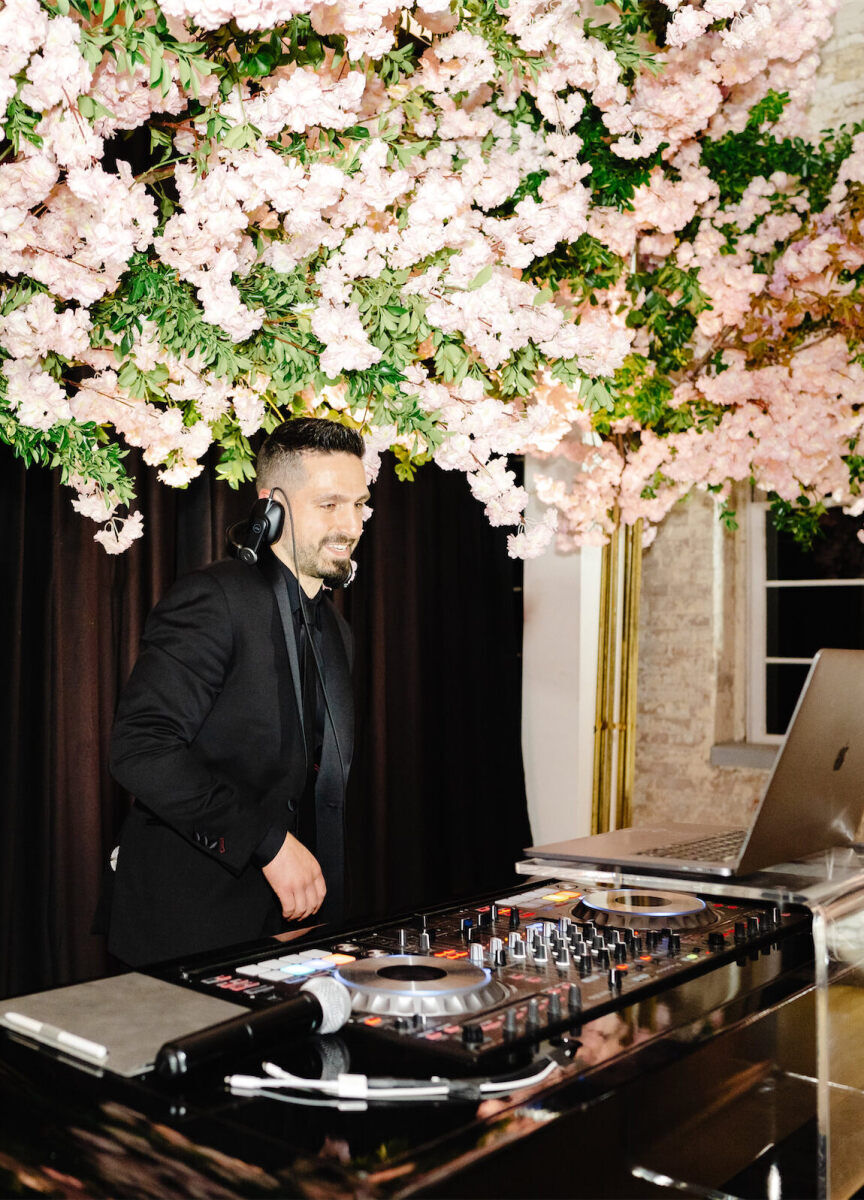 A DJ plays music under an installation of soft pink flowers at an art museum wedding.