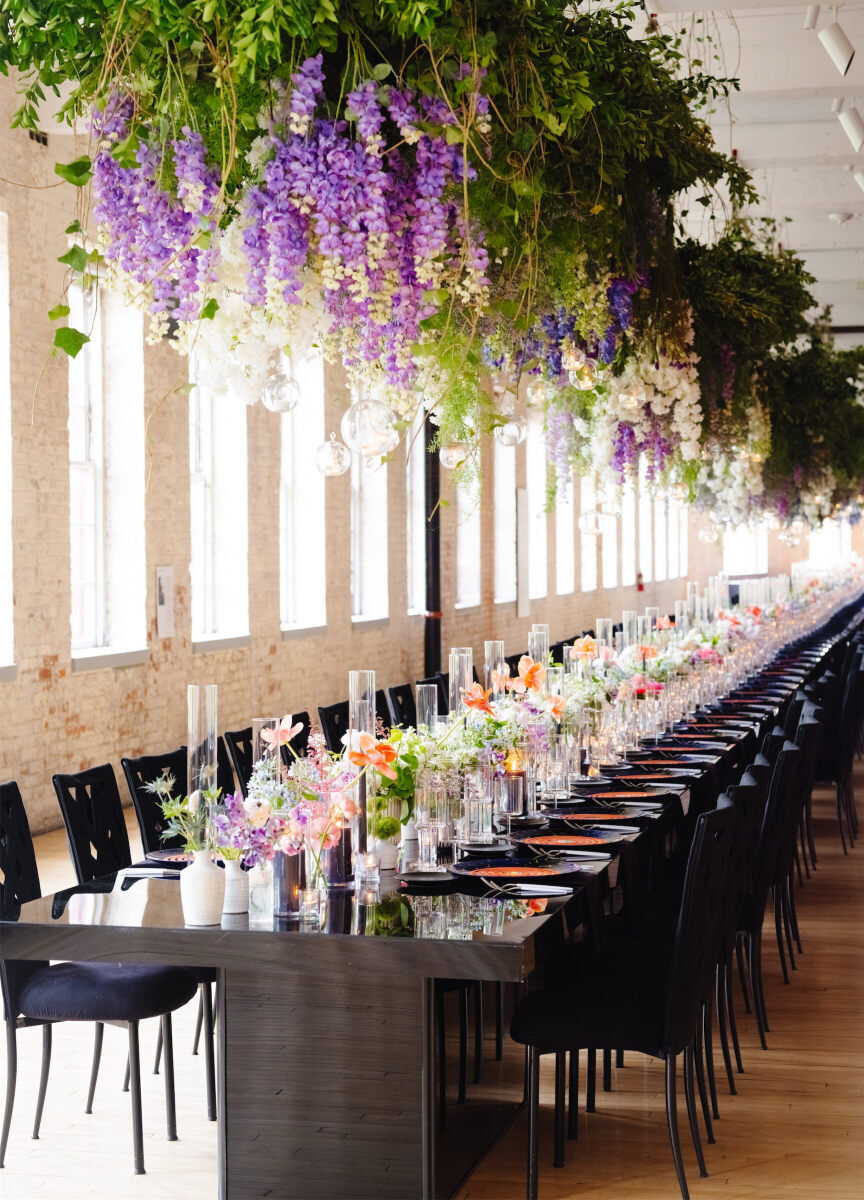 Greenery and dripping floral hung above the long table at an art museum wedding reception, which had a modern design incorporating black rental pieces and art-inspired menus.