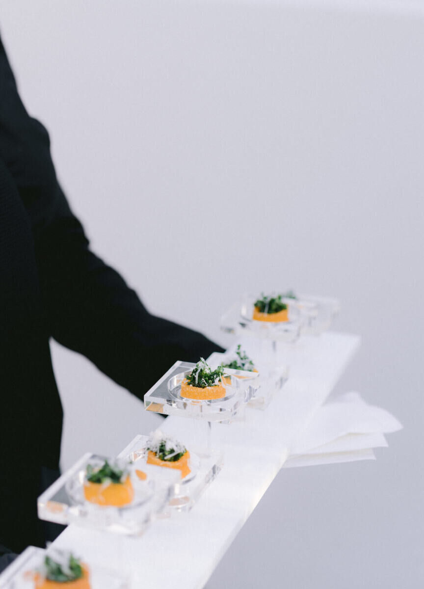 Appetizers being served on a lucite-tiered tray at an at-home wedding.