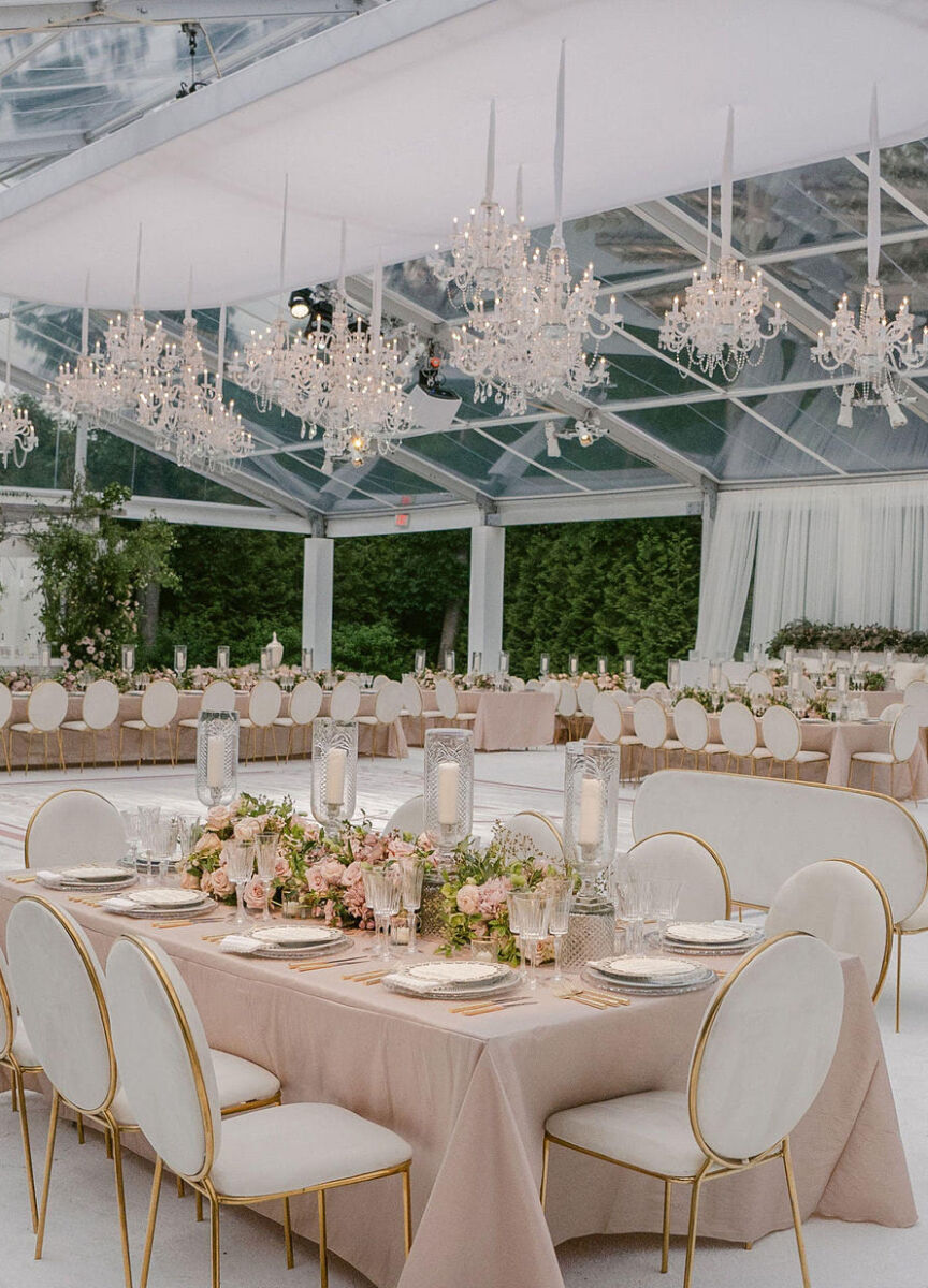 Clear top tented pink and white wedding reception featuring crystal chandeliers.