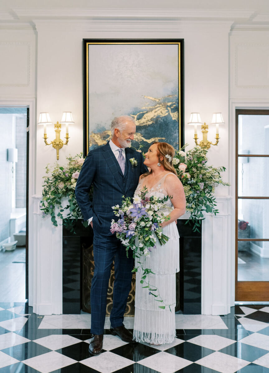 A groom and bride pose for a wedding portrait in front of the floral-covered fireplace inside their St. Louis home.