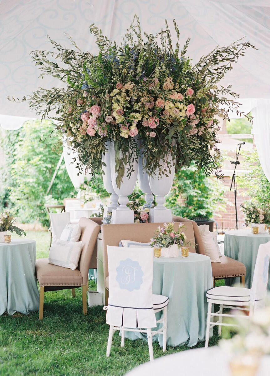 A towering floral arrangement that provides a focal point in the reception tent of a backyard wedding.