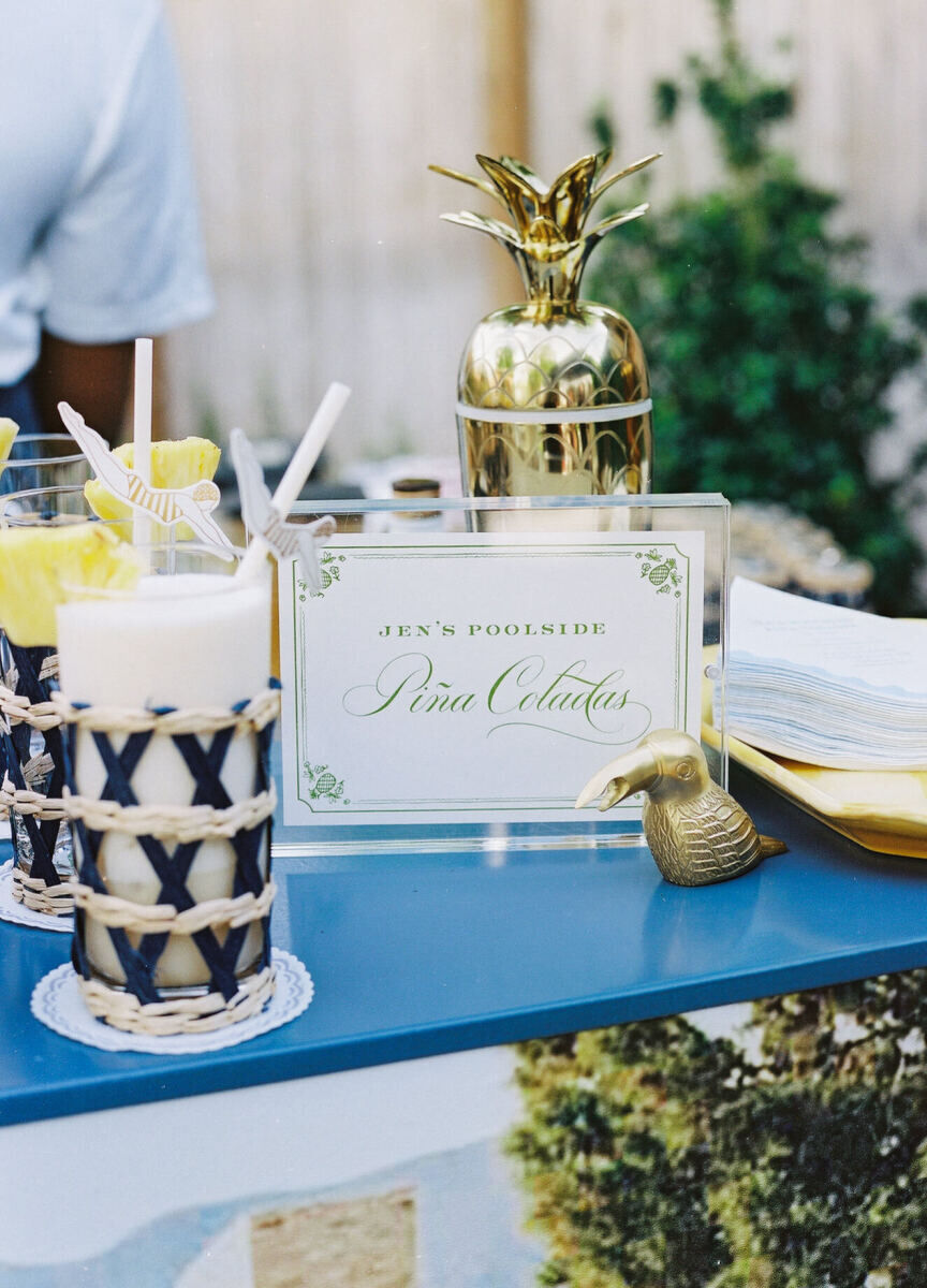 A piña colada bar at a wedding reception includes a pineapple cocktail shaker and paper synchronized swimmer straws.