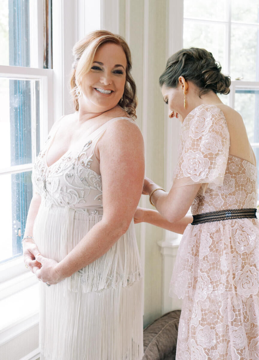 A smiling bride is zipped into her wedding dress.