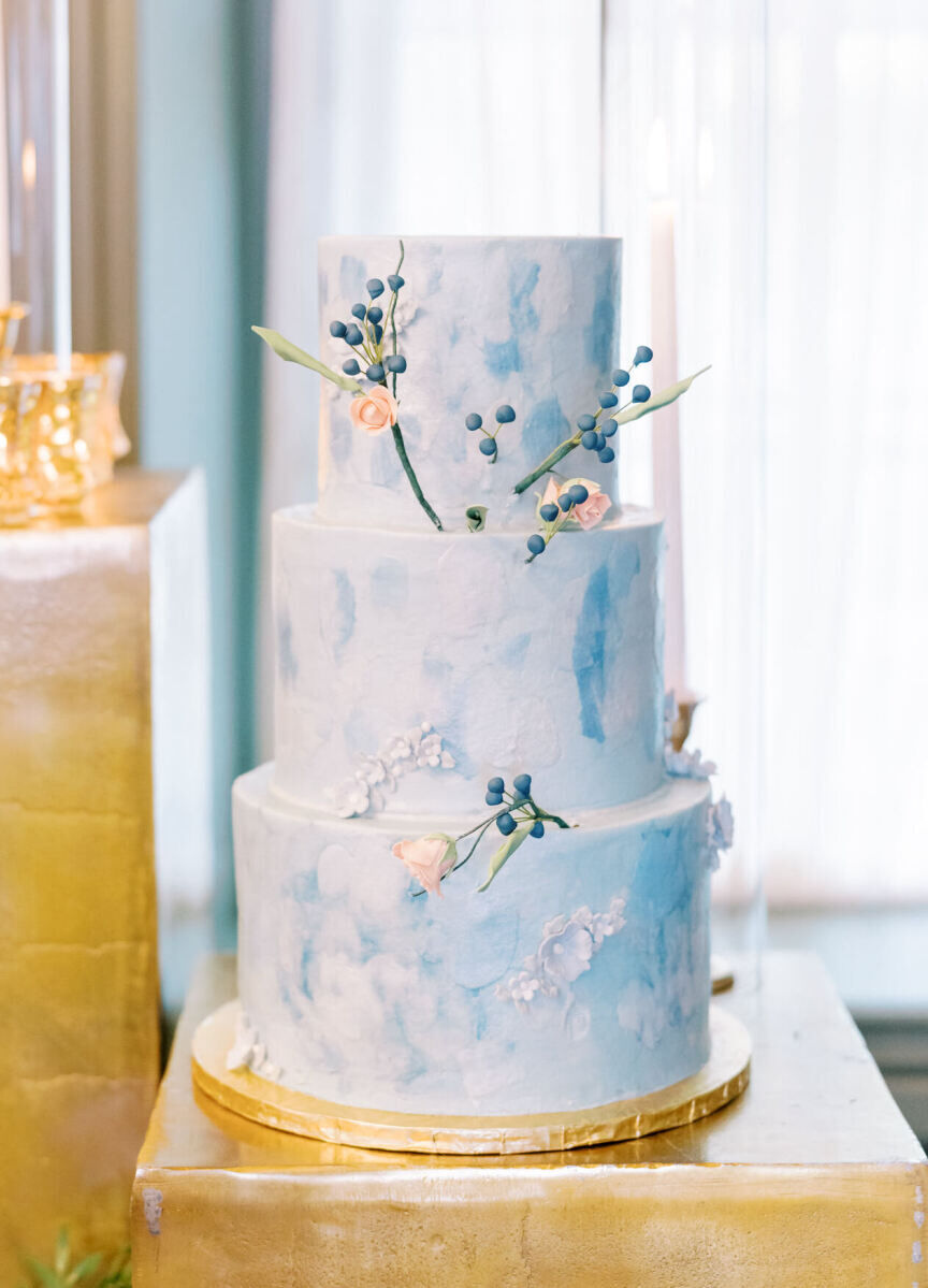 A textured, soft blue wedding cake with pink sugar flowers.