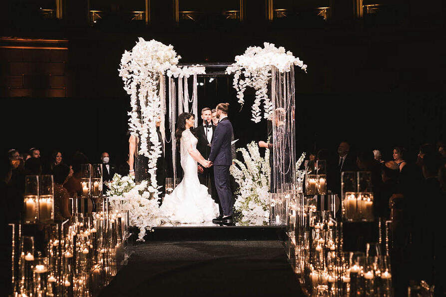 Ballroom wedding details: A candlelit aisle leads to an orchid-covered chuppah, under which a couple exchanges their vows.