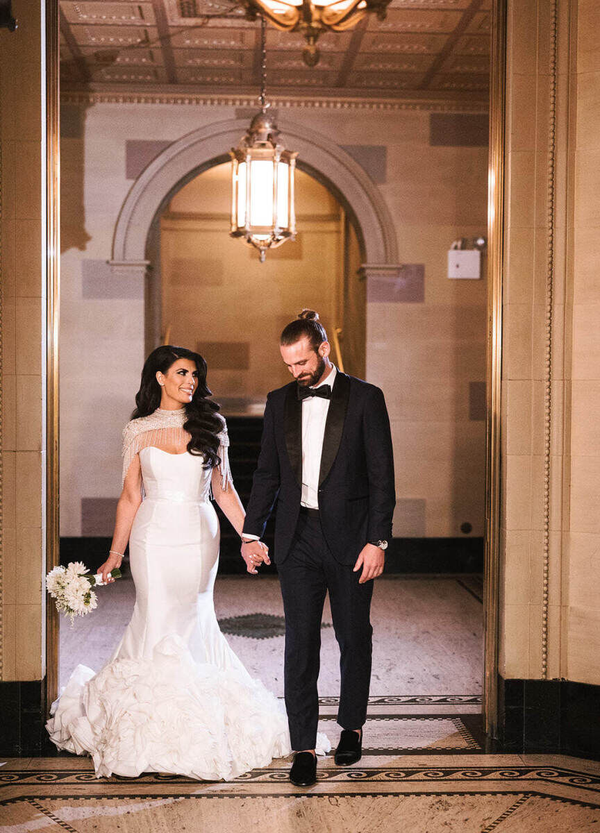 Ballroom wedding details: A bride holding her white bouquet and groom's hand inside their ballroom wedding venue.