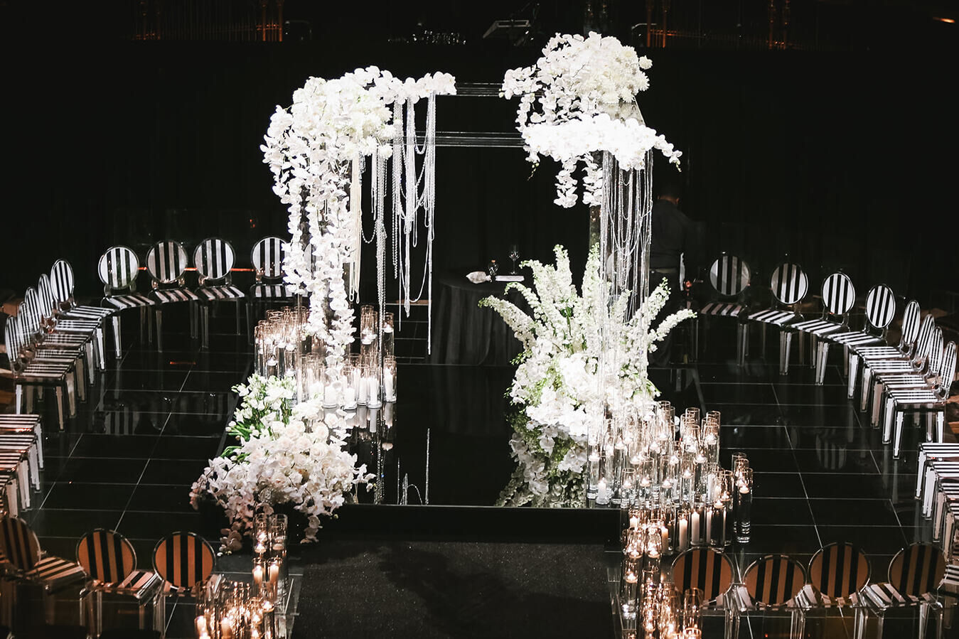 Ballroom wedding details: Clear, striped chairs surround a glamorous chuppah decorated with strands of white flowers and beads.