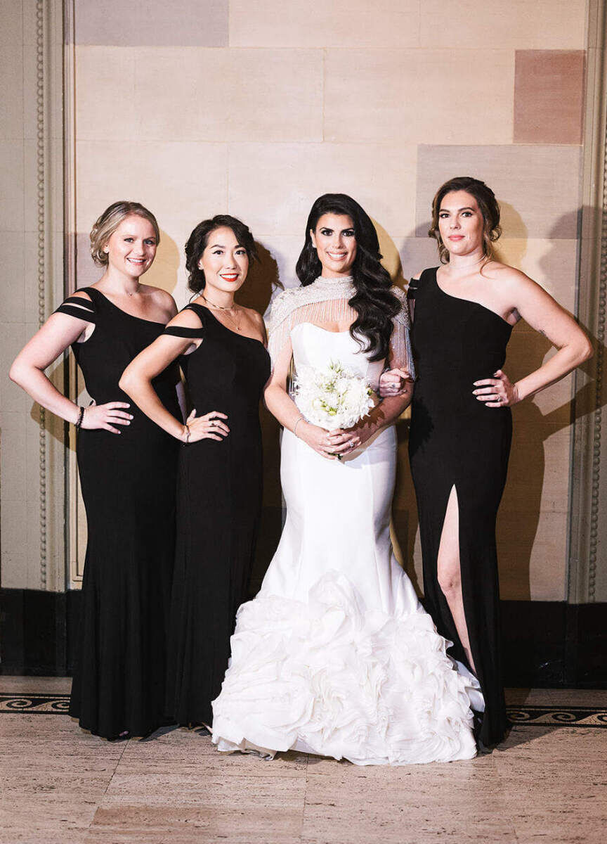 Ballroom wedding details: A bride poses with her three bridesmaids, wearing long black dresses.