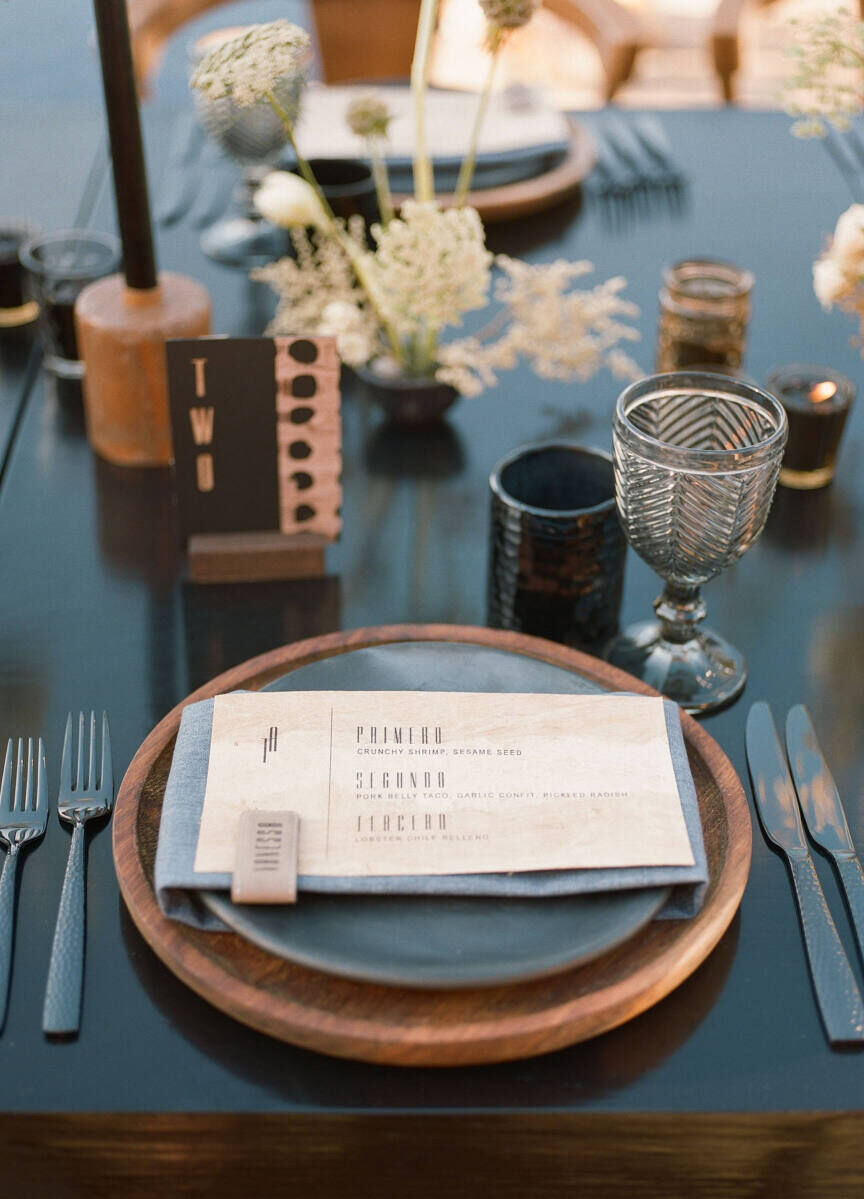 A modern-meets-bohemian wedding reception calls for wood chargers, black matte plates, leather-accented menus, and a mix of candles and floral arrangements between place settings.