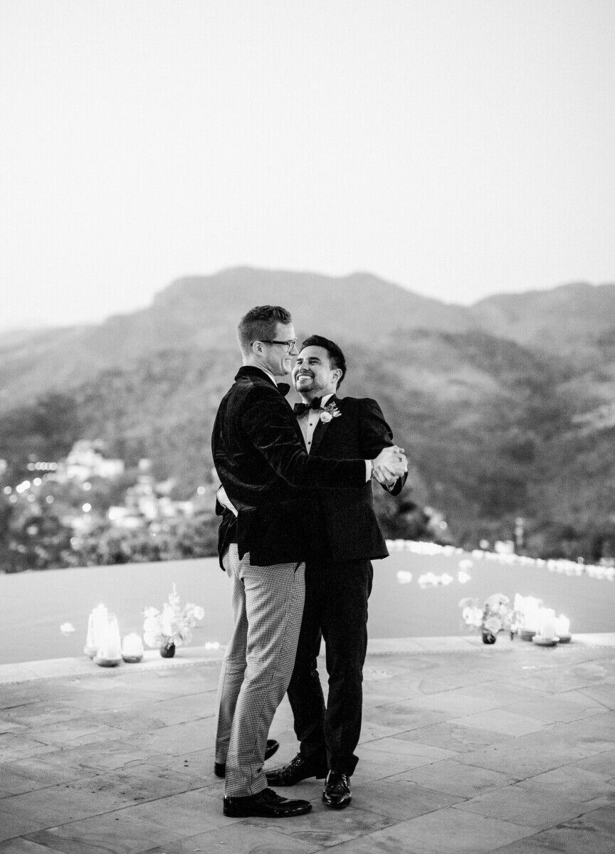 Wedding couple dances on outdoor balcony overlooking valley, surrounded by candlelight
