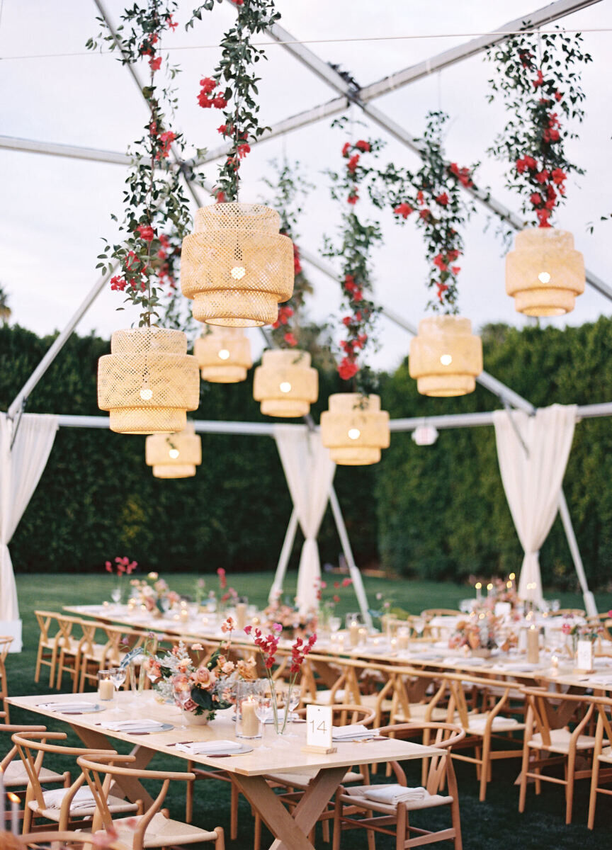 Ceiling Wedding Decor: A white outdoor tent with woven rattan light fixtures and greenery hanging above long rectangular tables.
