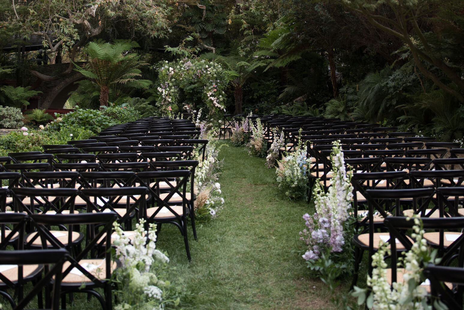 Celebrity Wedding: An outdoor ceremony setup with black chairs and floral arrangements along the aisle, leading up to an arch.