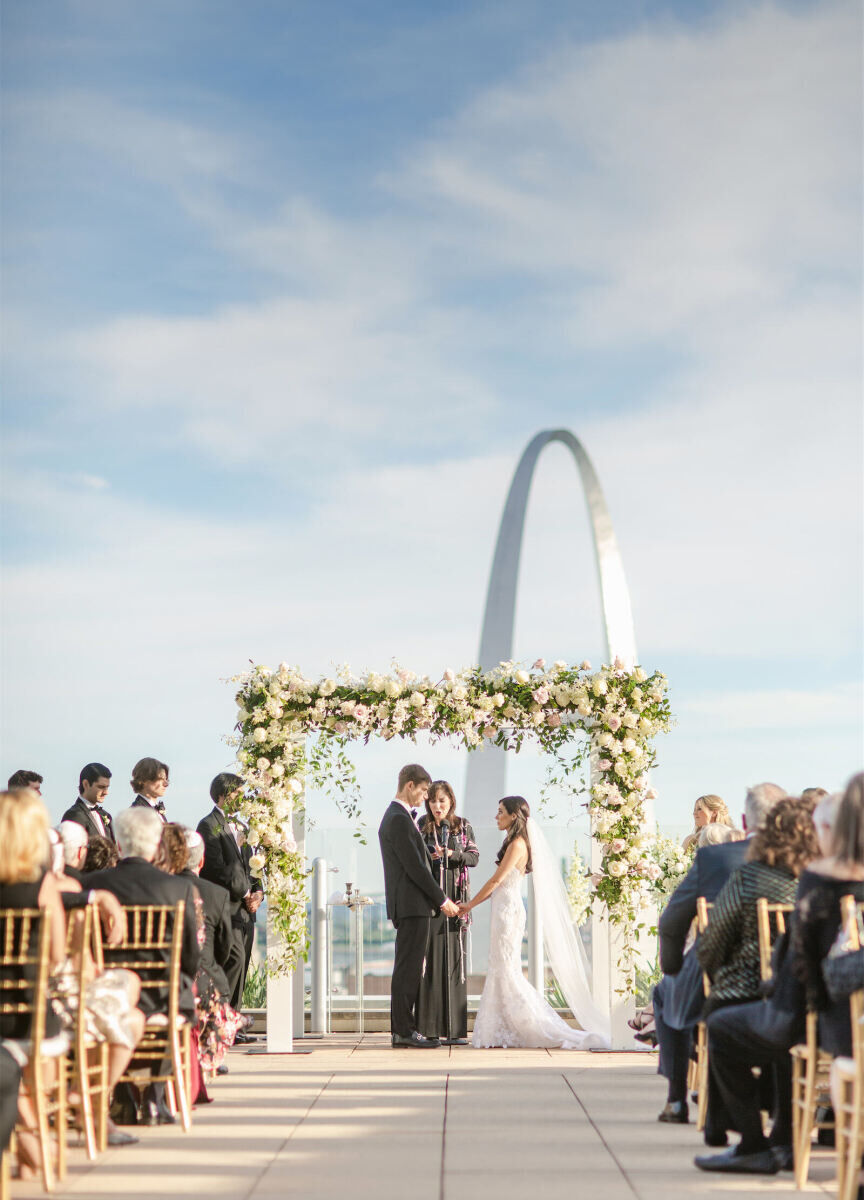 City Weddings: A couple holding hands during a rooftop wedding ceremony overlooking the Gateway Arch in St. Louis.
