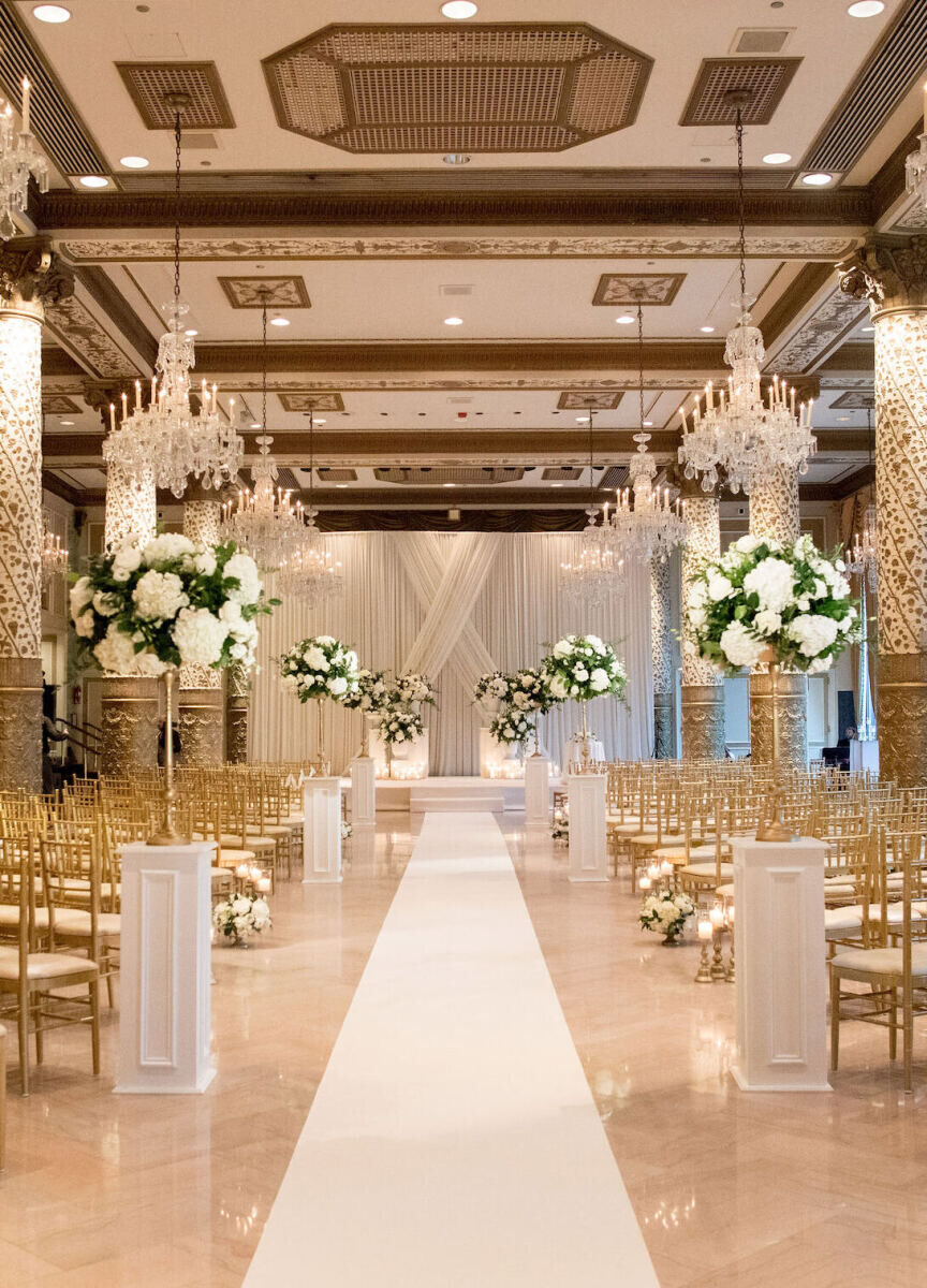 City Weddings: An opulent indoor ceremony setup with gold chairs and white pillars with floral arrangements lining the aisle at The Drake in Chicago.