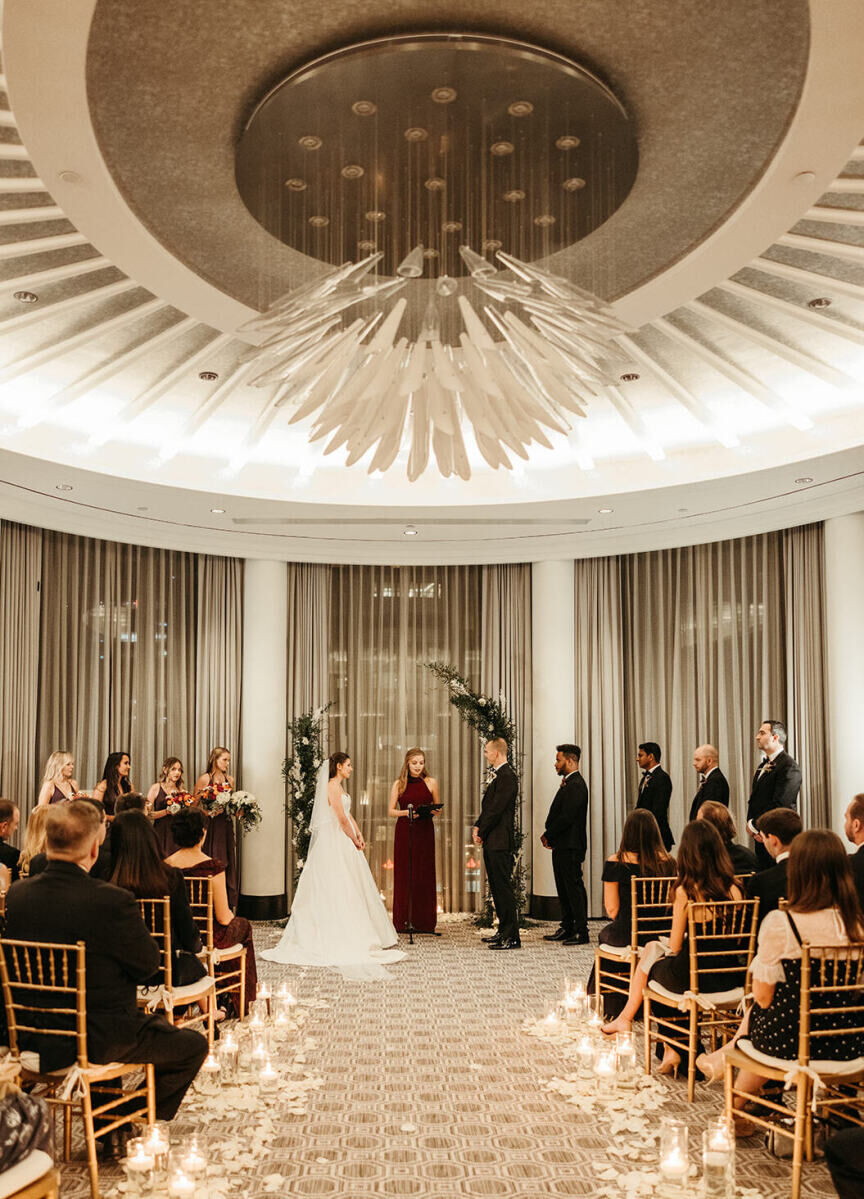City Weddings: A couple, their wedding party, officiant and guests at an indoor ceremony in the Four Seasons Hotel One Dalton Street in Boston.