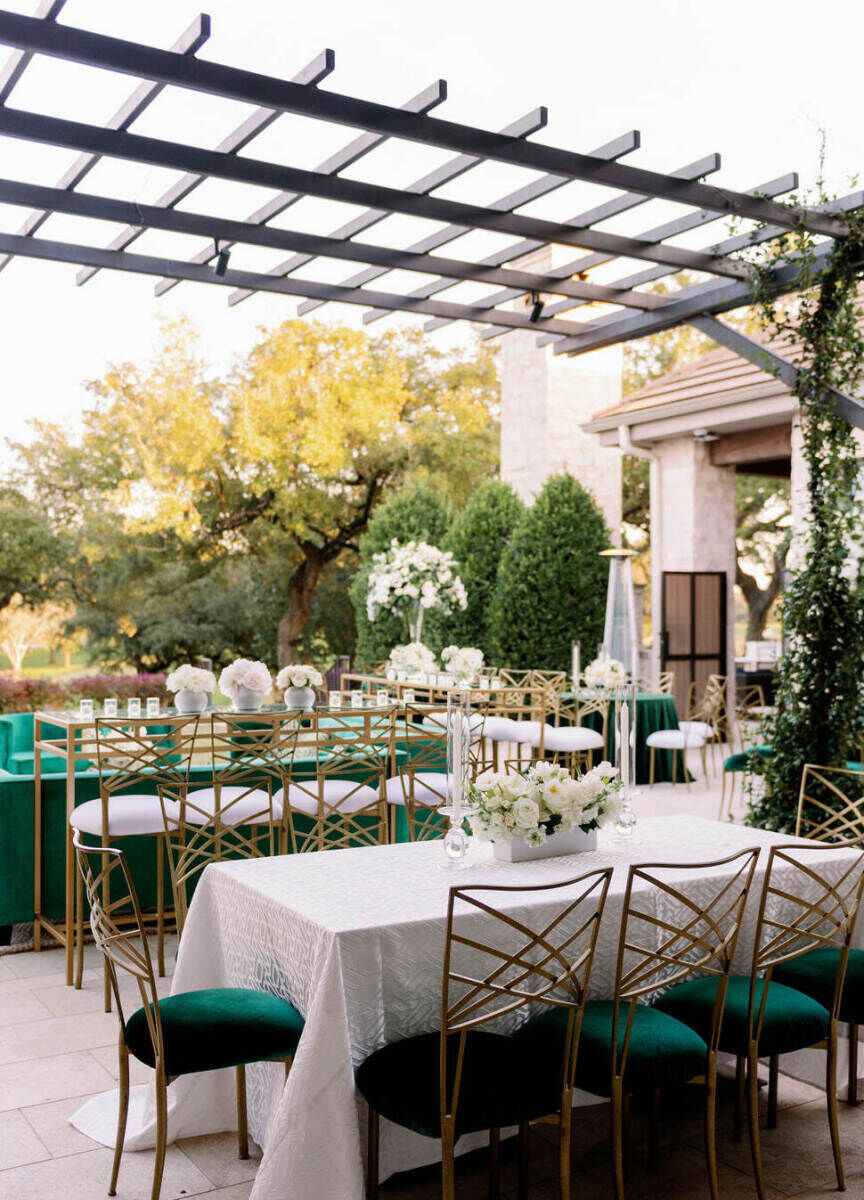 City Weddings: An outdoor reception area with rectangular tables, metal chairs with emerald green seat cushions and white floral arrangements.