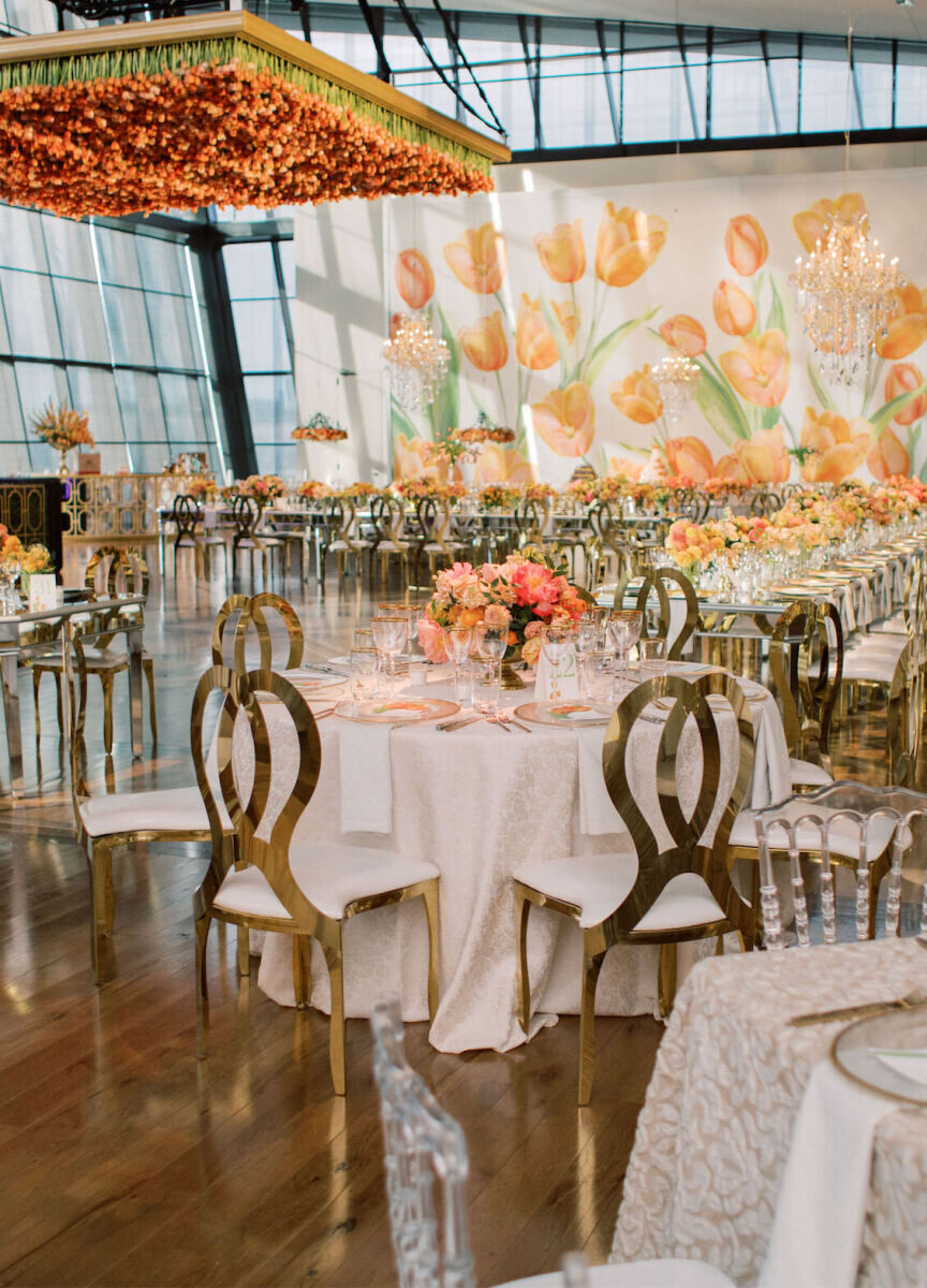 City Weddings: An indoor wedding reception setup with circular and rectangular tables, a hanging floral installation and yellow and orange floral motifs.