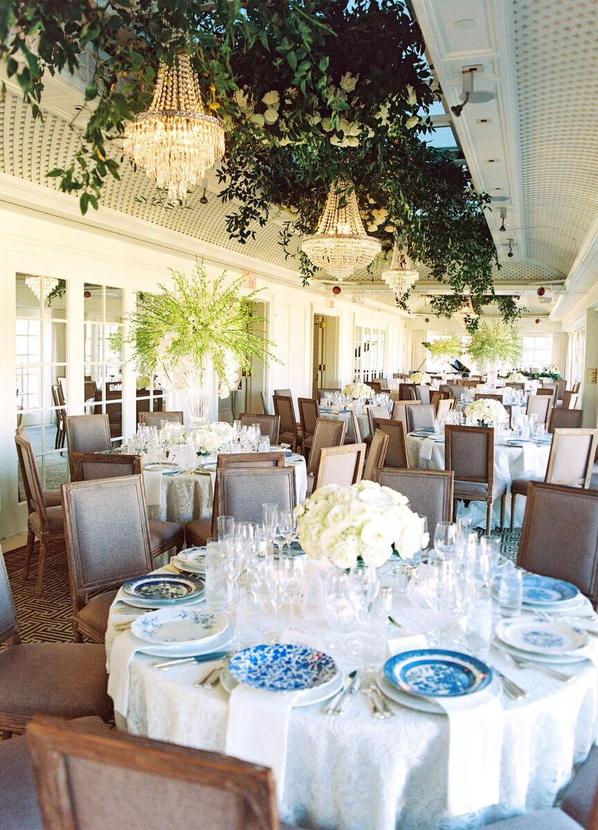 City Weddings: A reception setup with round tables, blue and white china and a hanging installation with greenery and chandeliers.