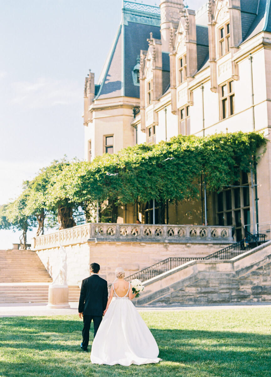 City Weddings: A wedding couple with their backs facing the camera, walking toward Biltmore, a historic mansion in Asheville.