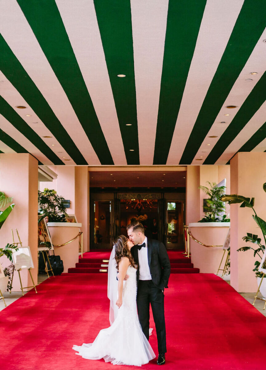 City Weddings: A wedding couple kissing at the entrance to the famous Beverly Hills Hotel, with a red carpet below and green and pink striped ceiling above.