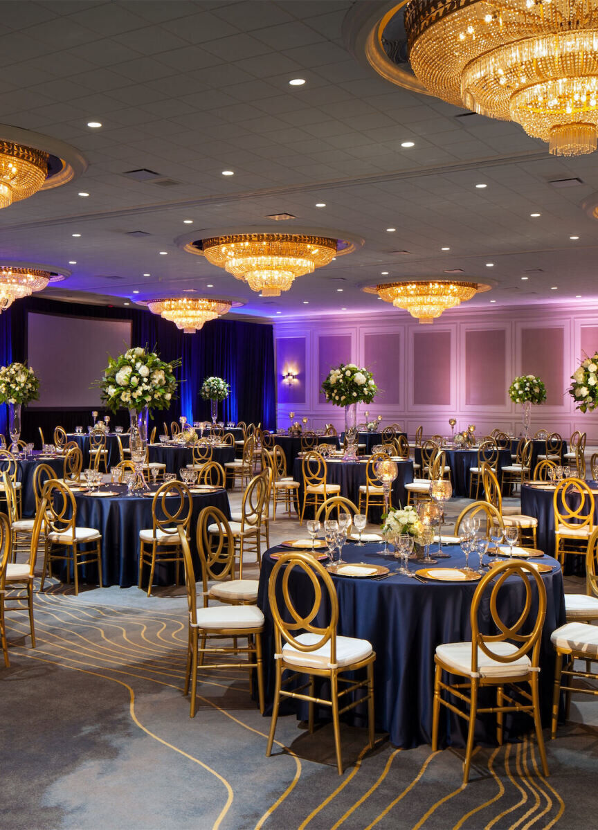 City Weddings: A yellow and purple indoor reception setup with circular tables, gold chairs and chandeliers above.