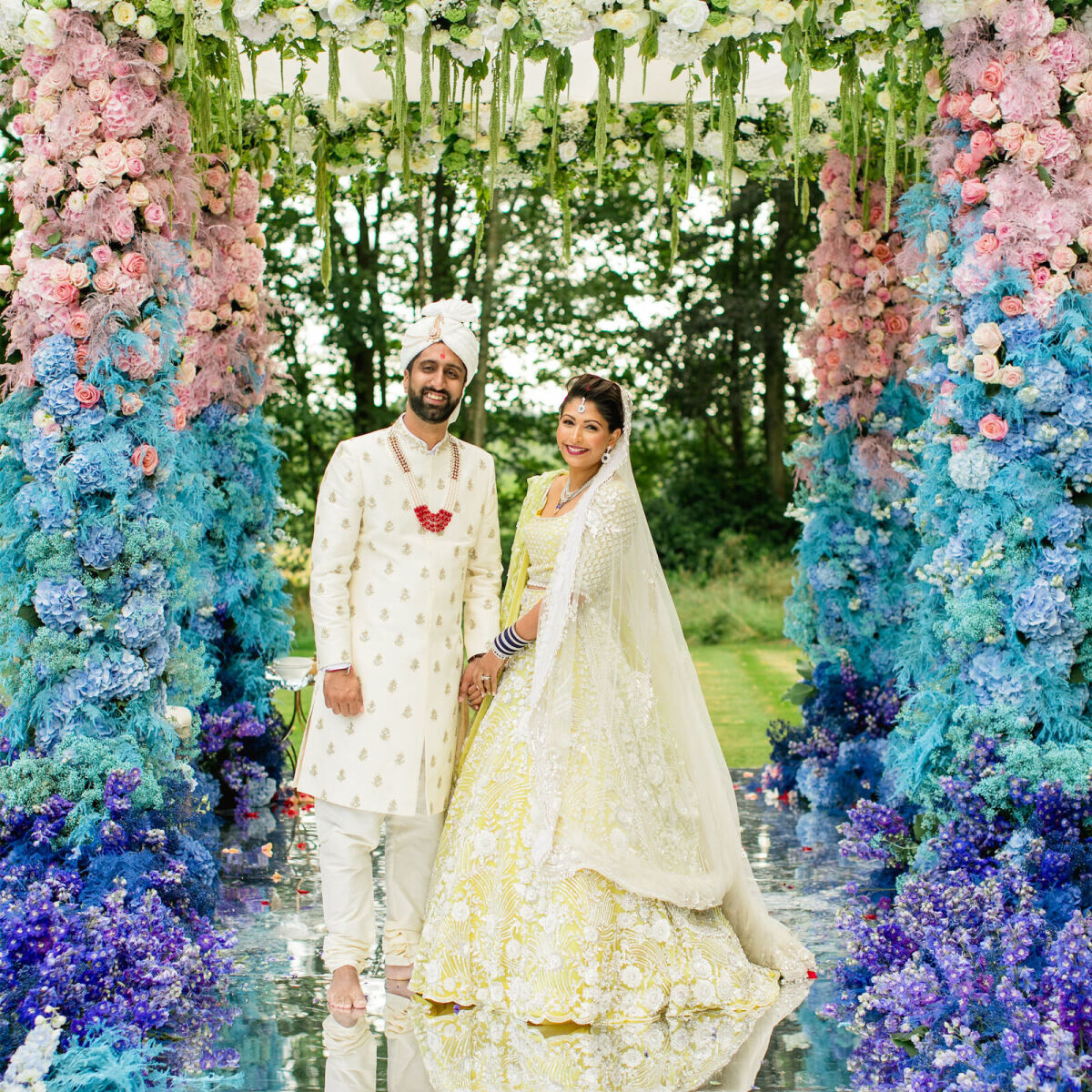 A groom and bride smile under their mandap at their beach-inspired colorful countryside wedding in England.