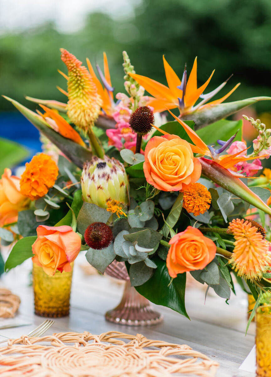 An assortment of orange flowers decorated tables at a colorful countryside wedding luncheon.