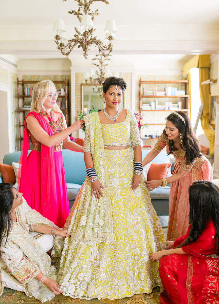 A bride in a yellow lehenga, surrounded by her bridesmaids, preps for her colorful countryside wedding.