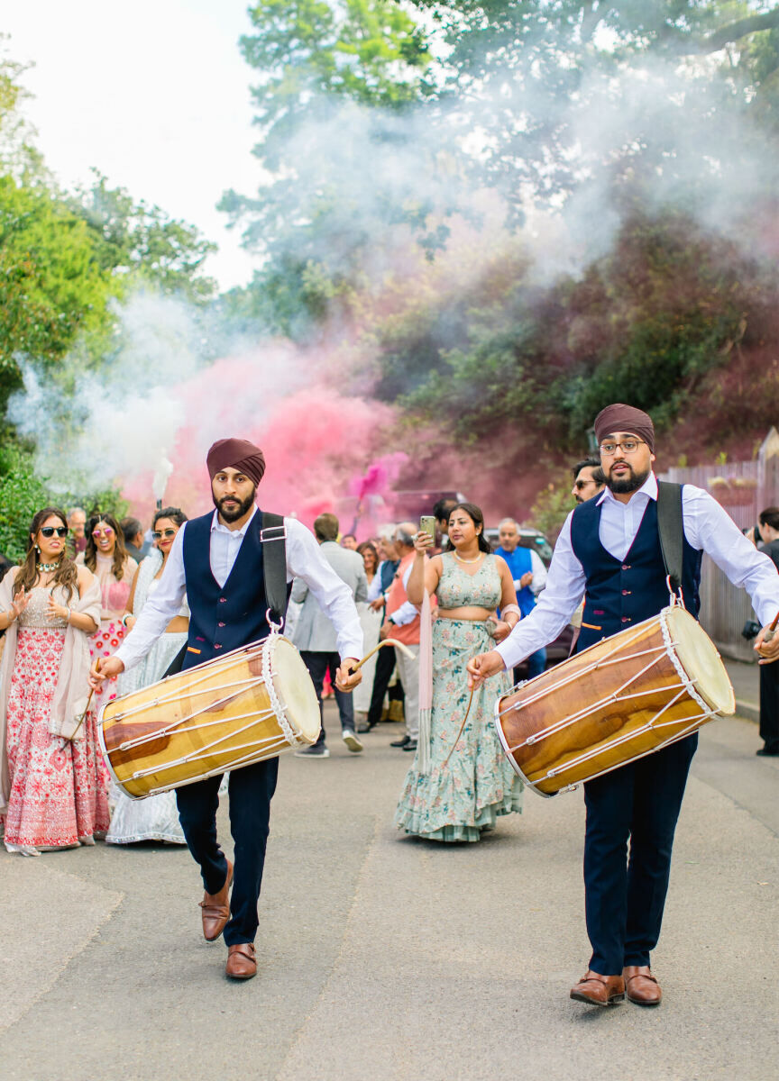 Dhol drummers play as smoke bombs add shades of pink to the air during the baraat that kicked off a colorful countryside wedding.