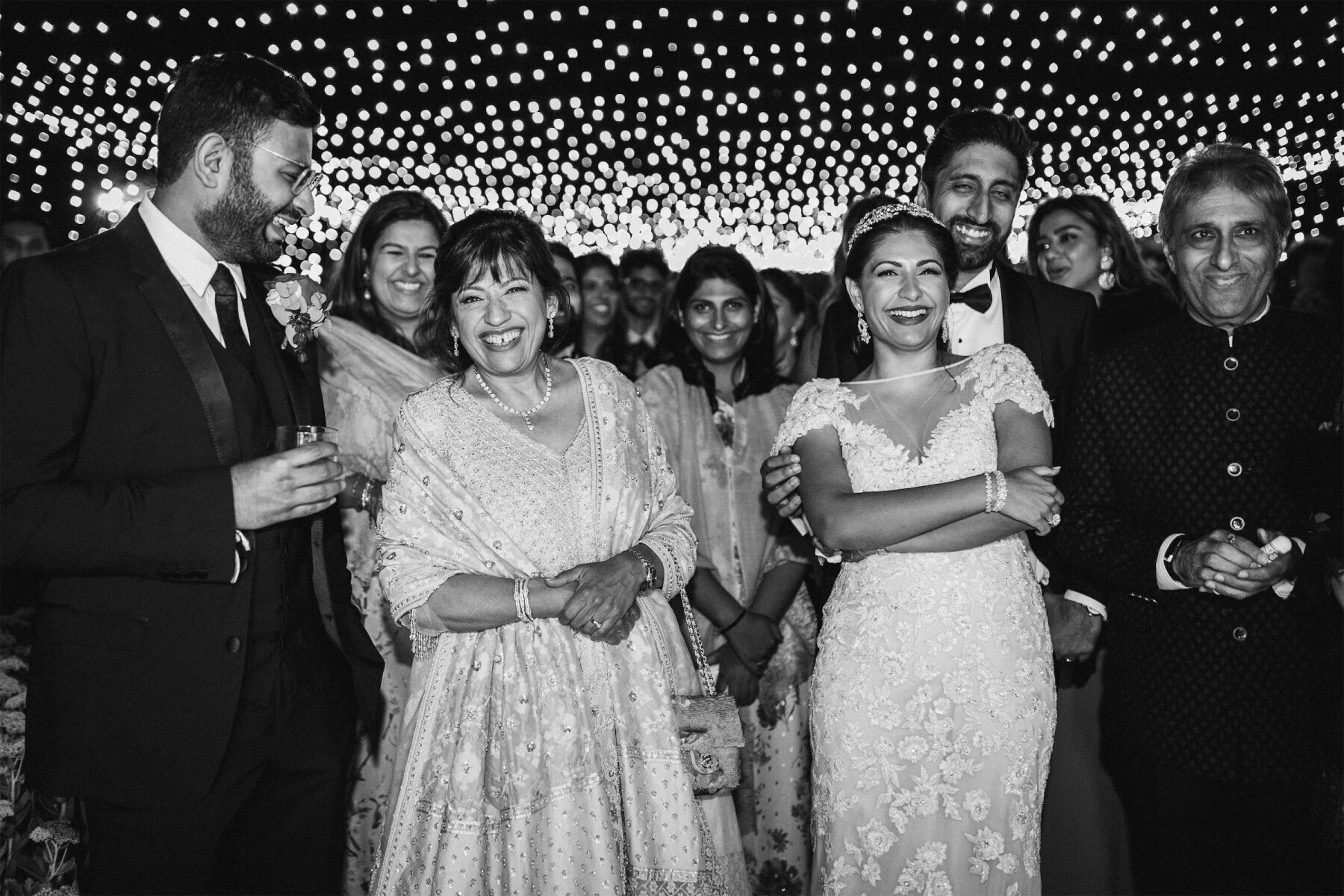 Newlyweds and their loved ones smile at the edge of the dancefloor at their indoor reception that was one of the final events of their multi-day colorful countryside wedding weekend.