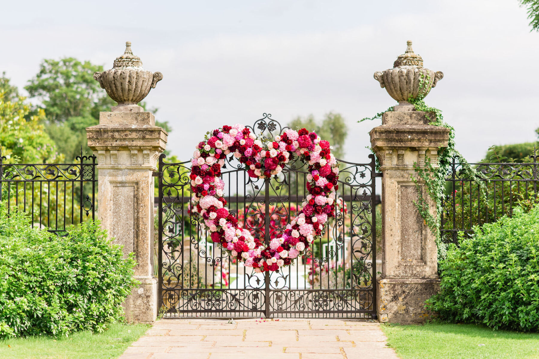 A pink-and-red heart-shaped wreath decorates the gates of the Four Seasons Hampshire for the first day of a colorful countryside wedding.