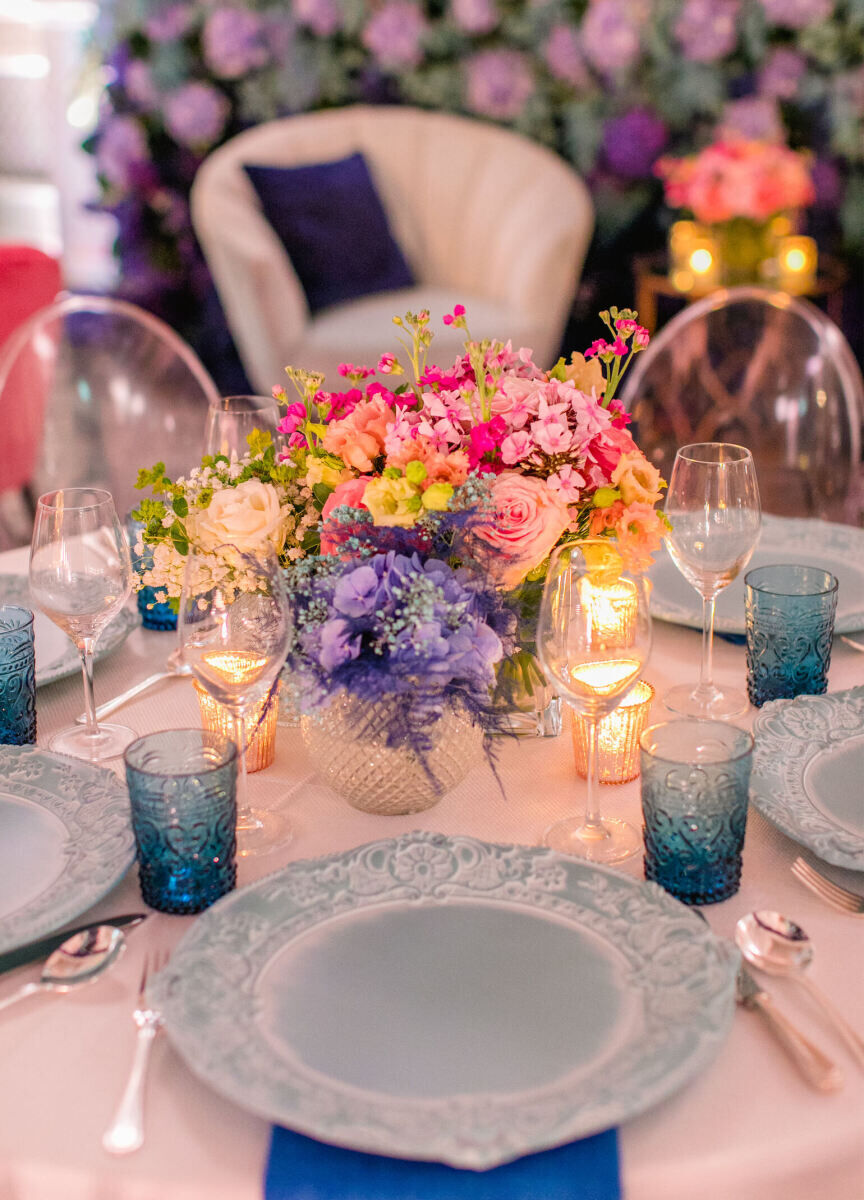 Blue napkins, pale turquoise chargers, aqua glasses, and vibrant floral centerpieces decorated the reception tables of a colorful countryside wedding reception in England.