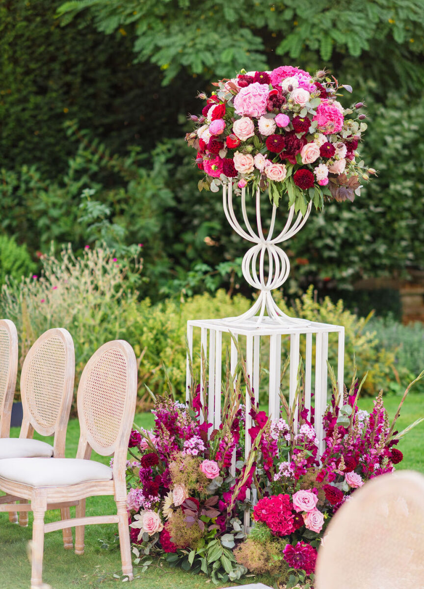 A colorful countryside wedding ceremony was decorated with red and pink flowers behind the last row of chairs.