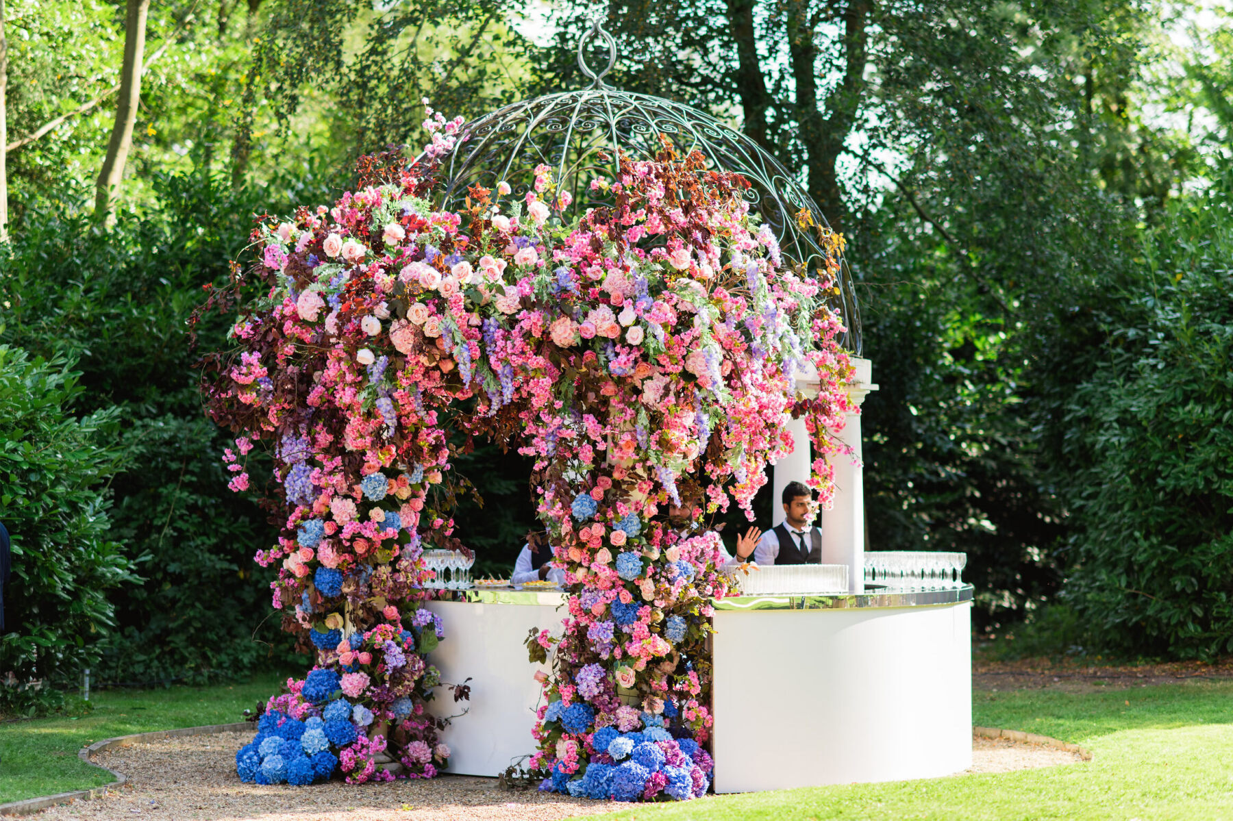 Pink, blue, and purple flowers decorate the bar of a colorful countryside wedding reception.