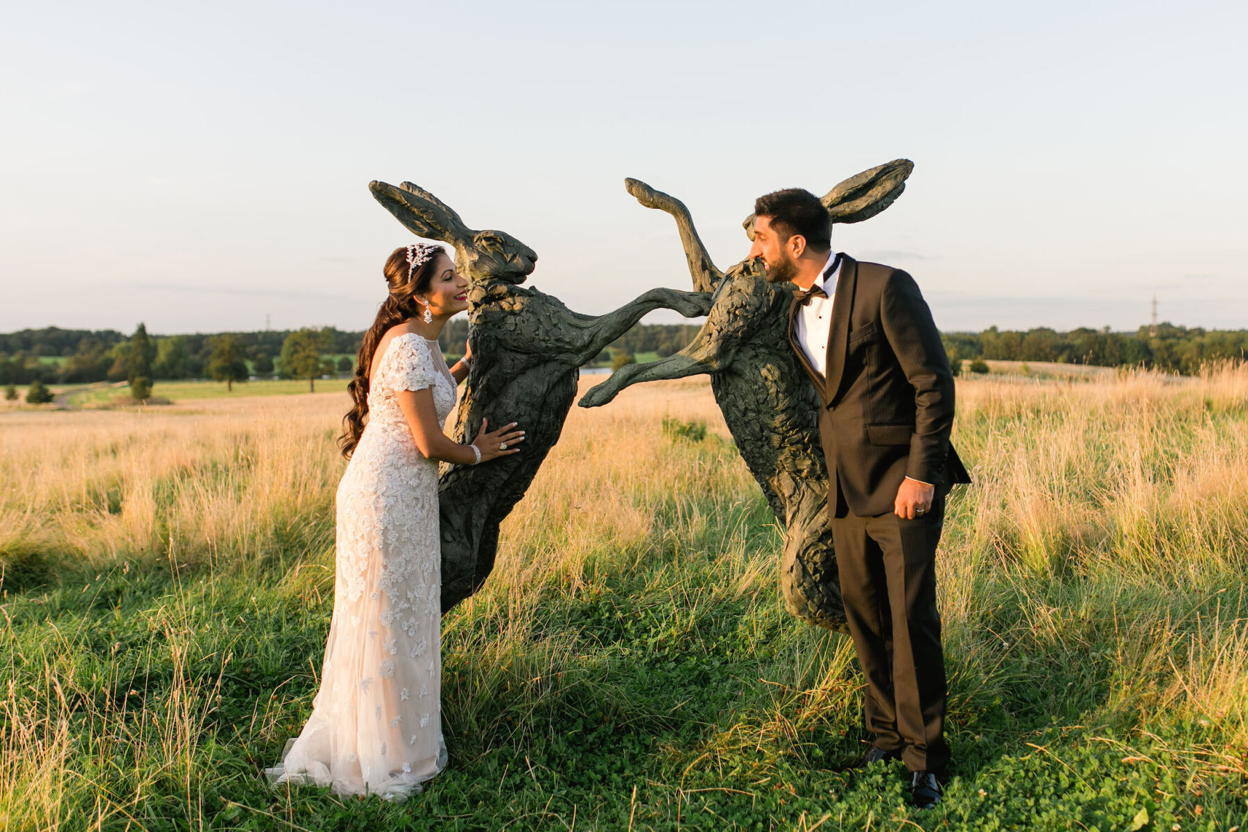 A bride and groom pose with large rabbit sculptures on the grounds of the Four Seasons Hampshire, where they had their colorful countryside wedding.