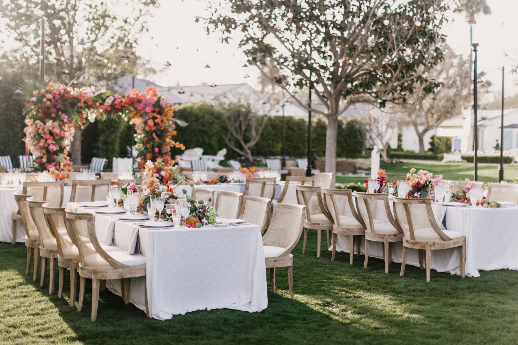 Colorful Wedding: A reception setup up with a colorful floral arch and rectangular tables with wooden and woven chairs.