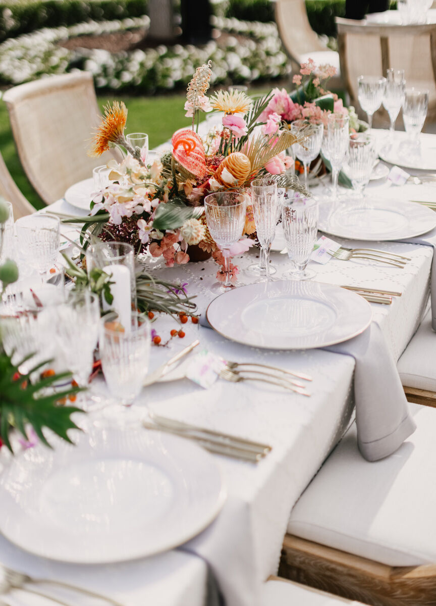 Colorful Wedding: An up-close look at a wedding tablescape with orange and pink floral arrangements and white linens and plates.