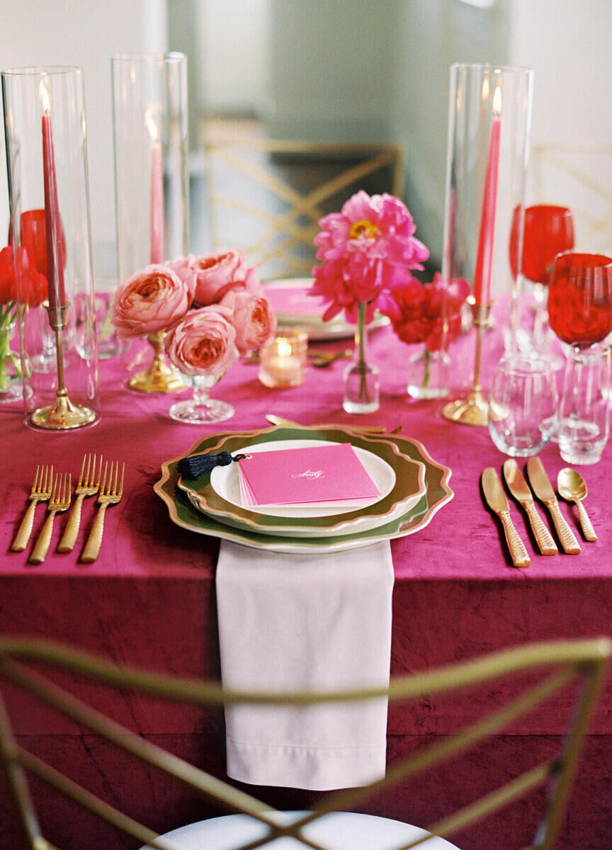 A placesetting, with multiple pieces of gold flatware for the multi-meal dinner reception, flank a stack of fluted green plates and a pink menu with a tassel on it.