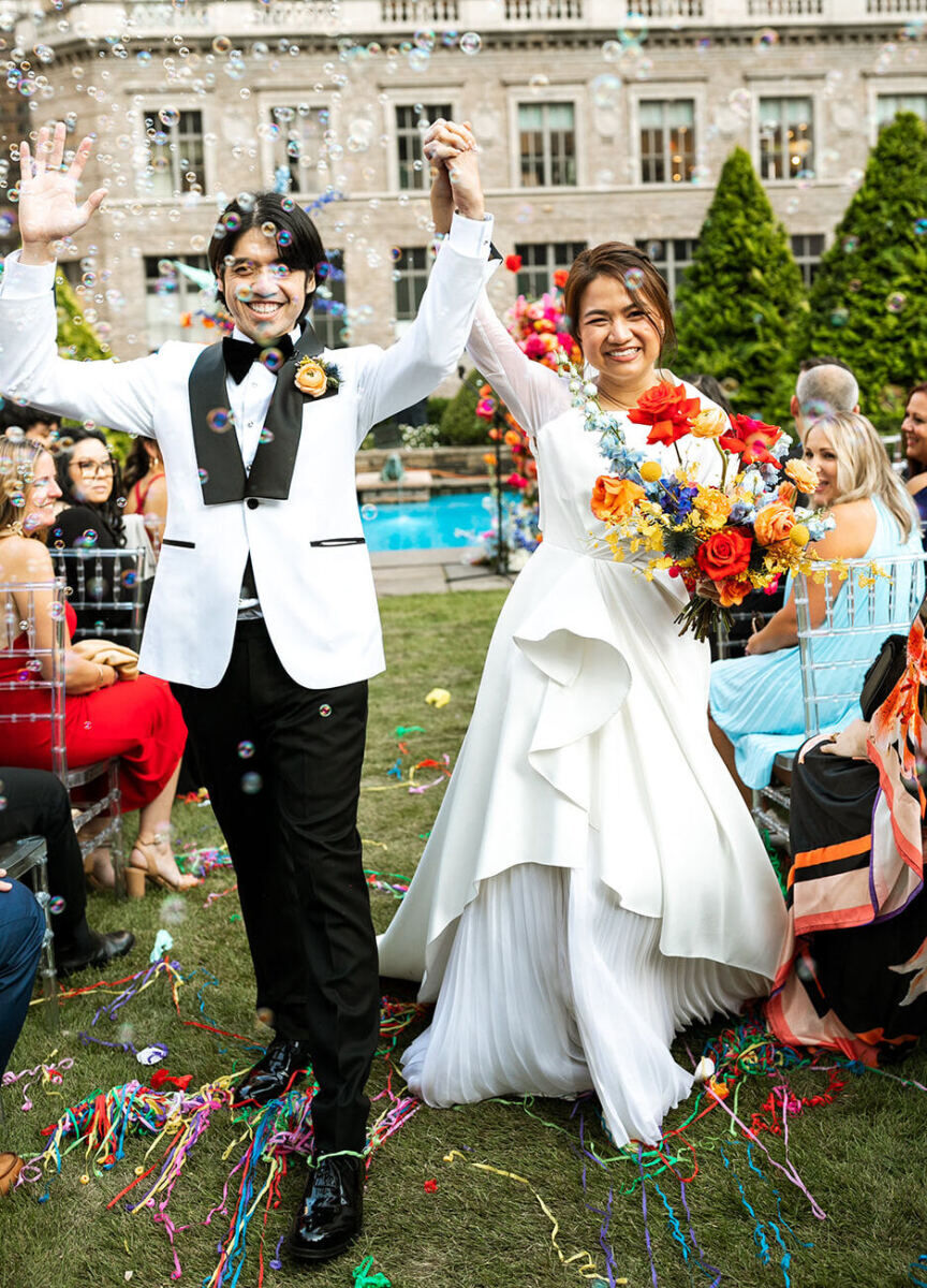 Best Places for a Colorful Wedding: A bride and groom smiling hand in hand, walking down a grassy rooftop aisle at 620 Loft & Garden.