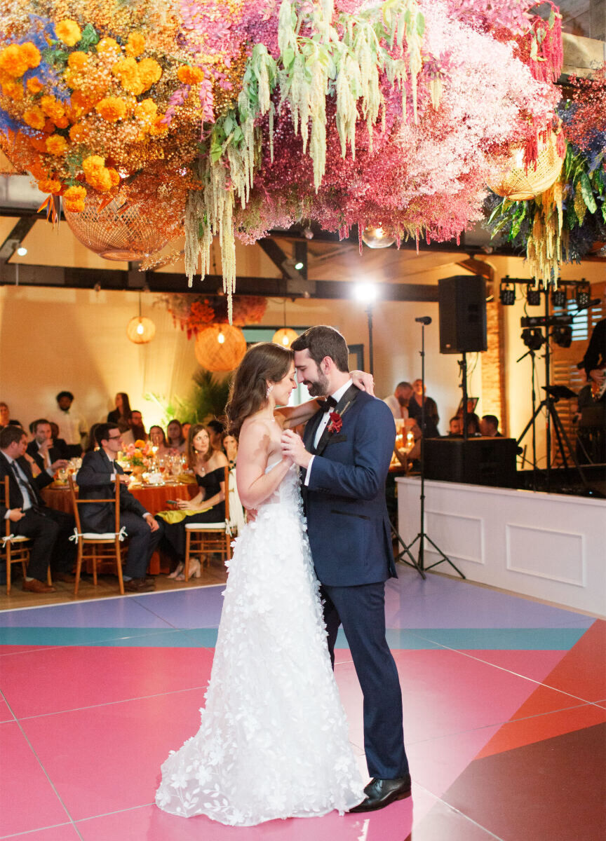 Best Places for a Colorful Wedding: Two newlyweds slow dancing on a colorful geometric dance floor with colorful florals hanging from the ceiling above them at Cannon Green.