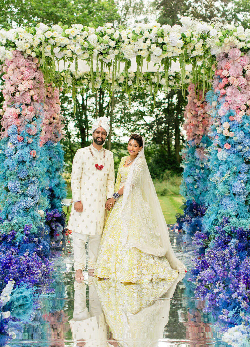 Best Places for a Colorful Wedding: A bride and groom smiling and holding hands on a mirror runway while surrounded by pastel-colored florals at Four Seasons Hampshire.