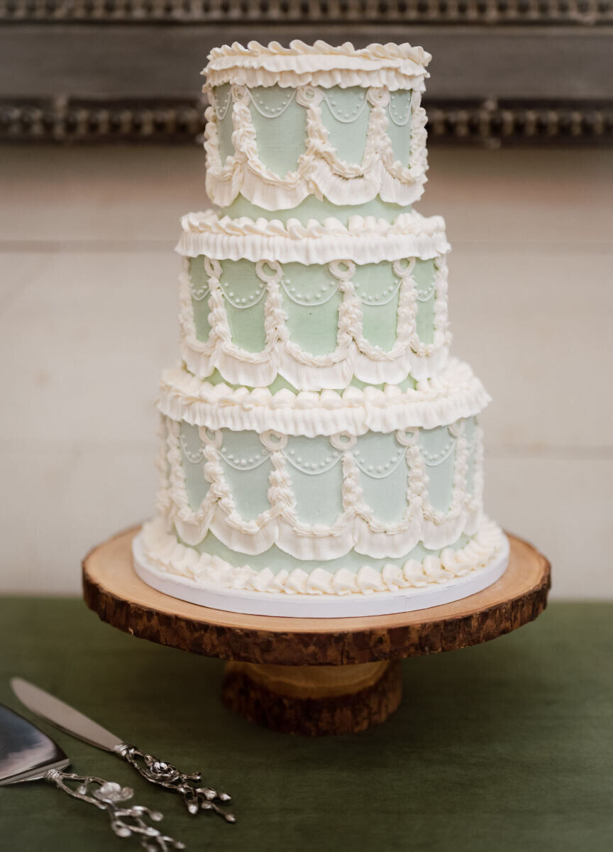 A vintage-inspired, pale green three-tier wedding cake piped with buttercrean and displayed on a wood cake stand.