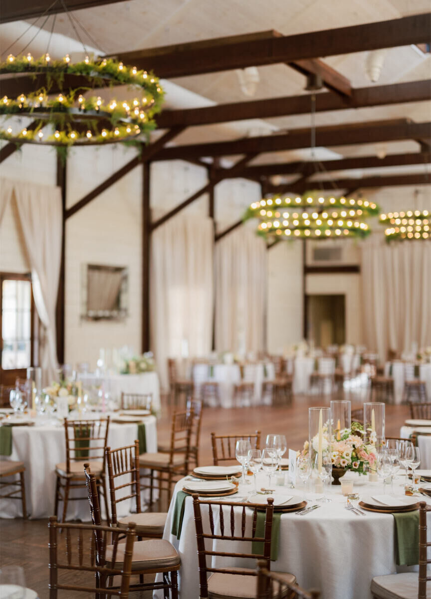 Inside the barn at Pippin Hill Farm & Vineyards, where a cottagecore wedding reception is set with round tables and brown chiavari chairs under the space's dark wood beams.